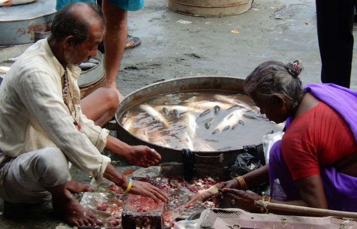 Two people cooking fish in a large bowl outside